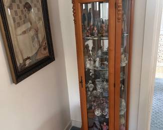 A 5 drawer lighted curio cabinet. on the left is a framed 'girl in a bathtub', NOTE the vintage alarm clocks on top and many small items including various Humels & Precious Moments in the cabinet. 