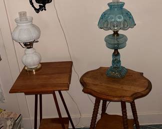 one square and one round top parlor tables. Milk glass hurricane lamp on the left and on the right a 'Moon & Stars' pattern ice blue table top lamp.