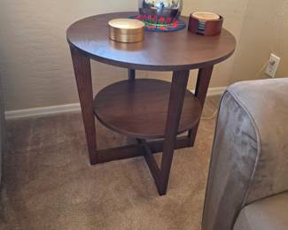 Round wood end table with lower shelf and modern cross-base design.
