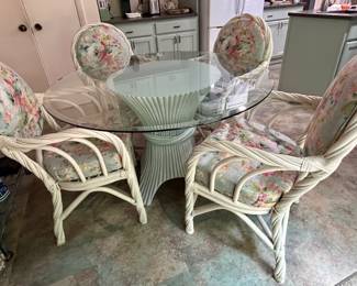 White rattan and glass-top dining set with floral-upholstered armchairs and a round glass table