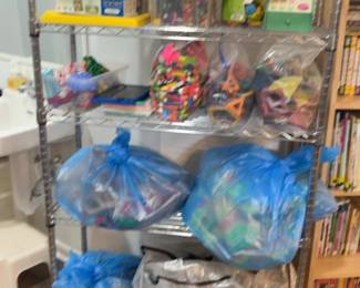 LE046 Wire shelving with assorted manipulatives and multiple large blue bags of classroom materials