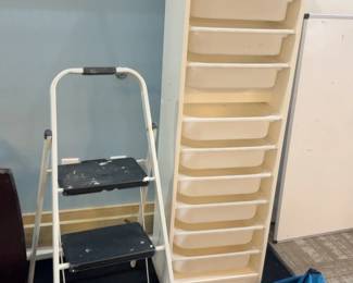 LE005 Folding step ladder beside tall stack of white classroom traysbins