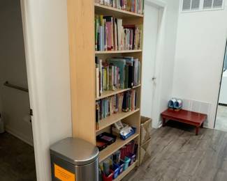LE047 Tall narrow wood bookcase with childrens books stainless step trash can nearby