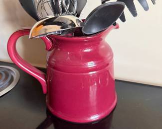 Red ceramic pitcher filled with black kitchen utensils
