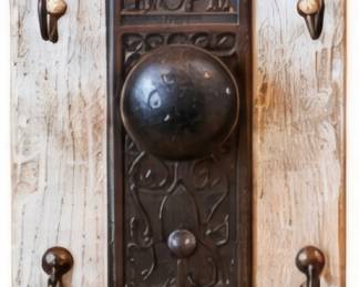 Rustic wall-mounted coat/key rack featuring a distressed white wood panel, four metal hooks, and an ornate vintage-style center plate with large knob and “HOPE” detail.