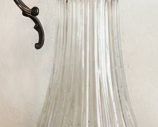 Vintage ribbed glass pitcher with ornate dark metal handle, lid, and spout.