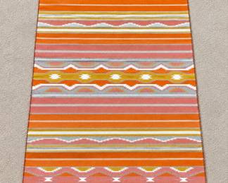 Southwestern woven rug with warm terracotta, coral and mustard tones, featuring repeating geometric patterns and decorative corner tassels.