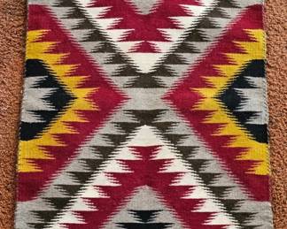 Southwestern-style woven rug with bold geometric diamond and stepped patterns in burgundy, mustard yellow, black, gray and cream.