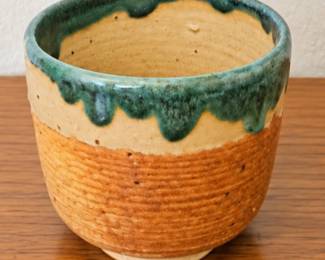Handcrafted pottery bowl with textured earth-tone finish and green drip glaze.