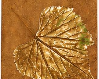 Square decorative wall plaque with a raised metallic gold leaf design.