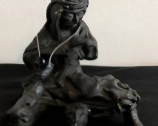 Dark carved sculpture of a seated figure riding a stylized animal.