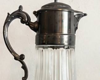 Vintage ribbed glass pitcher with ornate dark metal handle, lid, and spout.