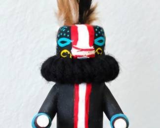 Handcrafted Kachina-style figure with feathered headdress, bold black, red and white painted details, yarn accents and traditional-style garments.