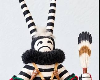 Black-and-white striped Kachina-style figure with tall horns, black fur collar, colorful yarn accents, feathers and geometric apron.