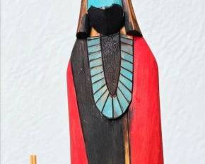 Tall slender Kachina-style figure with turquoise, red and black painted details, holding a bundle of reeds.