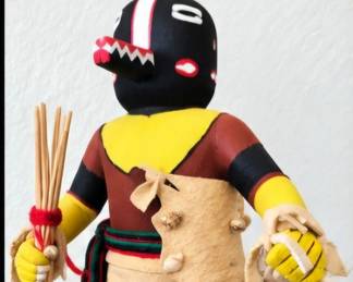 Handcrafted Kachina-style figure with black mask, bright yellow accents, leather-style garments, moccasins and bundled reed accessories.