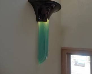 Vintage "Purcell Sconce" designed by Karl Springer in the 1980s, featuring a dark metal fixture paired with an illuminating hand-chipped aqua glass insert crafted by artist Joseph Spohr. Multiples available