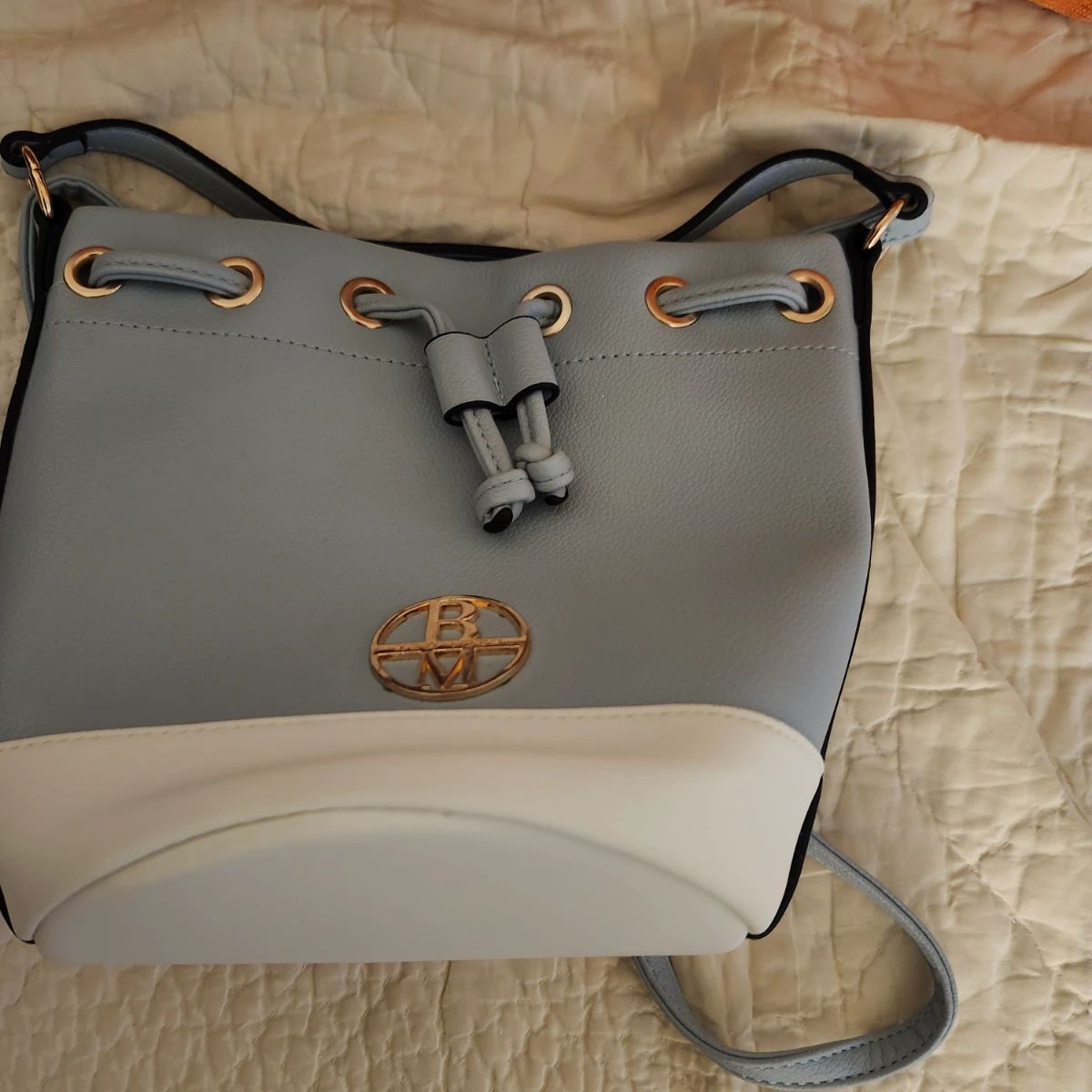 This is a light blue and white colorblock bucket bag by Badgley Mischka New York from the Rae collection, featuring gold-tone hardware and a drawstring closure