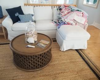 White slipcovered sofa with chaise; drum coffee table; area rug