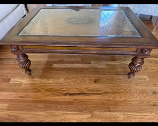 Ethan Allen British Classics Glass-Top Coffee Table - 44" x 36". Substantial traditional coffee table from Ethan Allen's British Classics collection. Rich arm-brown wood finish with an inset beveled glass top over a decorative woven/caned panel, carved apron with rosette detailing, and heavily turned/fluted legs with brass-toned feet/ casters. The wood and glass are in good overall condition.