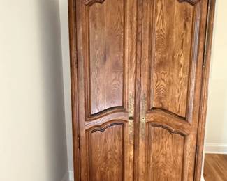 French Provincial/Louis XV-style carved wood armoire or wardrobe. Two-door featuring a arched crown, carved floral and foliate detailing across the crest and lower apron, raised panel doors, decorative brass hardware and short carved cabriole-style feet.