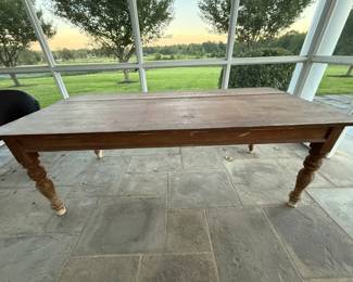 Rustic Farmhouse Dining Table with Turned Legs: substantial wood farmhouse table with a warm, naturally aged finish and classic turned legs. The long rectangular top has visible grain, surface wear and variations in the finish that give the table an authentic rustic, collected-over-time appearance. Statement piece for a farmhouse or country home. Ideal as a work table too.