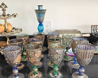 IMPORTANT MURANO JUDAICA CEREMONIAL GLASS COLLECTION Exceptional collection of elaborate Jewish ceremonial glass acquired by the owner in Murano, Italy, at a reported original cost of approximately $22,000 including shipping. The collection comprises numerous individually decorated Kiddush goblets and monumental ceremonial glass, incorporating Magen David, menorahs, Torah and other Judaic imagery with elaborate floral and foliate ornament, applied glass elements, enamel, and extensive gold and silver/platinum-colored decoration. The collection closely relates in form, iconography and decorative technique to rare Murano Jewish ceremonial glass documented in the 2018 scholarly publication Judaica. Murano Glass. Private Collection, which illustrates approximately 300 examples of late-19th and early-20th-century Venetian/Murano Judaica. Exact dating of the present collection remains under research.