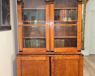 Authentic 19th-century Biedermeier architectural bookcase/cabinet in highly figured birch veneer, with a dramatic stepped cornice, Gothic Revival pointed-arch glazed doors, ebonized architectural accents and carved detailing. The upper glazed bookcase rests on a two-door cabinet base, both displaying exceptionally strong flame/curly figuring throughout. A monumental and visually striking period European cabinet combining classic Biedermeier cabinetry with Gothic architectural elements.