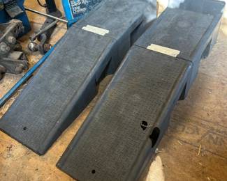 Plastic Car Ramps with Quik Grip Tire Chains This lot includes a pair of black plastic automotive car ramps with diamond-tread surfaces for tire traction. One ramp has a visible hole or damage point on the top surface that should be noted. Also included is a blue hard-sided case of Quik Grip tire chains. Plastic car ramps are a garage staple for oil changes and undercarriage access, and the tire chains add winter driving readiness to the lot. Sold as found.