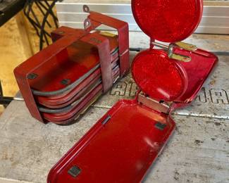 This vintage road emergency reflector set includes multiple folding red reflectors stored in a compact metal carrying case with a spring-loaded handle. The reflectors fold flat for storage and pop open on hinged stands for roadside visibility. The red-painted metal cases show age-appropriate patina and wear, giving this set a classic mid-century look that appeals to both practical use and vintage auto accessory collectors.
