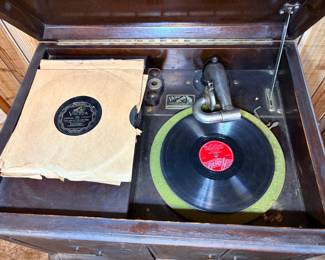 This antique Victor Talking Machine phonograph features a dark mahogany cabinet with a lift-top lid, a mechanical crank-wound turntable with green felt platter pad, and the original Victor tonearm and reproducer. A small collection of 78 RPM records is included — one visible sleeve reads Victor 22220-A, "Tuck Away My Lonesome Blues" by Jimmie Rodgers, a highly collectible early country recording. The Victor nameplate on the motor board confirms the maker. The cabinet shows age-appropriate wear and the mechanism is sold as found — working condition not confirmed.