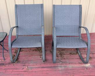 This pair of patio C-spring motion chairs features dark gray woven wicker-style seats and backs on curved steel cantilever frames. The spring-action base provides a gentle rocking motion, and the high-back design offers comfortable support for outdoor dining or deck lounging. Both chairs show light weathering consistent with outdoor use and have matching frames and fabric. A versatile pair of outdoor spring rocker chairs for a porch, patio, or deck.