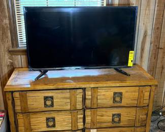 Hitachi Flat-Screen TV on Rustic 8-Drawer Wood Cabinet This lot pairs a Hitachi flat-screen TV with a rustic wood cabinet featuring eight drawer fronts with iron strap hardware and ring-pull handles in a distressed farmhouse finish. The cabinet's plank construction and iron accent details give it a southwestern or lodge-style aesthetic that works as a media console, entryway credenza, or bedroom dresser. The TV sits on top and shows a yellow energy sticker still attached. Working condition not confirmed on the TV — sold as found. This is a separate lot from the oak entertainment center with Hitachi TV (Lot 35) — two different furniture pieces, two different televisions.