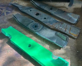 Lawn Mower Blade Lot — Used and New This lot includes four used lawn mower blades in gray steel showing surface rust and edge wear from normal mowing, plus one brand-new replacement blade still in green shrink-wrap packaging. Replacement mower blades are a recurring maintenance need for any homeowner with a riding or push mower, and having a spare new blade alongside serviceable used blades makes this a practical pickup for mower upkeep. Confirm blade lengths and center-hole patterns to match your mower deck.