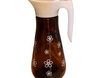 a vintage mid-century amber glass syrup dispenser with a white daisy pattern and plastic lid made by Thatcher Glass in the 1960s