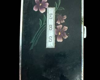 vintage Ronson Mastercase or Ronson Pal lighter and cigarette case combo. This iconic Art Deco piece dates back to the late 1930s to 1940s. The design features a black enamel body decorated with hand-painted purple flowers. It includes a central silver-toned monogram plaque personalized with the initials "EBS". The top left corner houses the signature Ronson automatic lighter mechanism, operated by a vertical textured thumb lever.