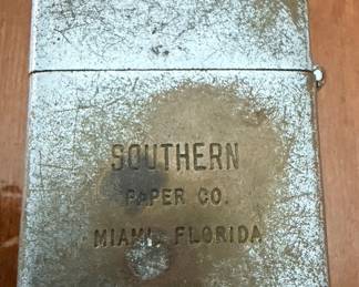 heavily weathered, vintage flip-top pocket lighter with promotional text engraved on the body: "SOUTHERN PAPER CO. MIAMI, FLORIDA".