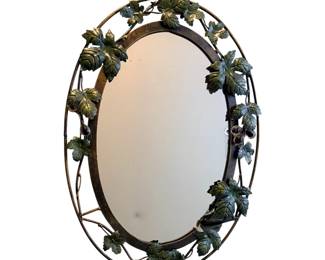 a vintage oval metal wall mirror featuring a decorative wrought iron sculptural grape vine and leaf frame.