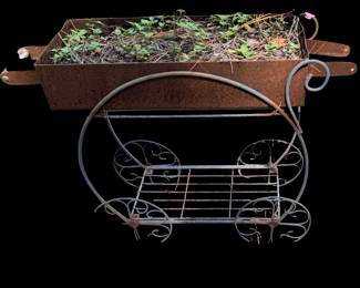 a rustic metal garden planter cart with scrolling scrollwork wheels and a lower wire shelf, similar to a Victorian-style flower cart