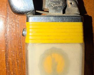 vintage Scripto Vu-Lighter from around the 1960s, featuring a clear fuel reservoir that lets you see the fluid level/ A clear and silver tone lighter with a yellow band and a paper insert that shows the Statue of Liberty and highlights The Independent Life & Accident Insurance Company of Jacksonville, Florida (Home Office).
