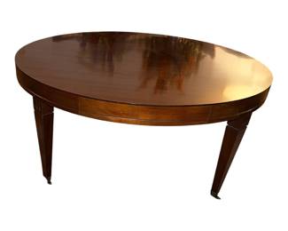 This is a vintage oval mahogany coffee table featuring a high-gloss polished finish, a deep apron, and classic square tapered legs equipped with brass caster wheels at the feet. This elegant design is very characteristic of mid-20th-century traditional furniture makers. 