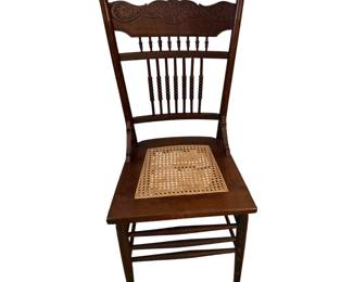 This antique wooden chair features a beautifully carved floral press-back crest and a classic woven cane seat.