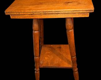 This is an oak antique two-tier oak parlor table featuring a square top, turned spindle legs, and a lower open display shelf.