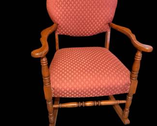 a vintage wooden rocking chair featuring a rounded upholstered backrest and seat with a textured red geometric pattern