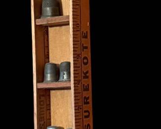 a handmade vintage vertical display shelf crafted from a wooden ruler, holding a collection of small metal thimbles