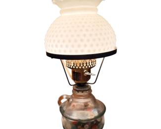 This is a vintage electric hurricane table lamp featuring a white milk glass hobnail shade with a ruffled top and a clear glass base filled with colorful  buttons 