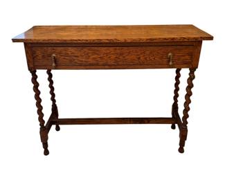 an antique English oak writing desk or side table, circa early 20th century, featuring characteristic barley twist legs, a single drawer, and brass pendant drop handles.  Circa 1910