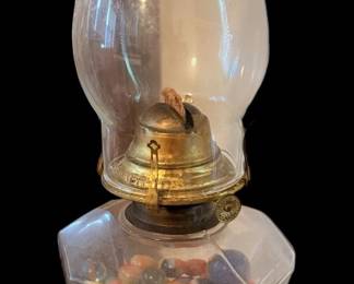 a vintage or antique clear pressed-glass oil lamp featuring a decorative fuel reservoir filled with colorful marbles