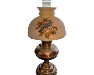 A vintage oil lamp desk/table lamp featuring a rounded frosted glass half-shade decorated with a hand-painted blue bird perched on oak leaves