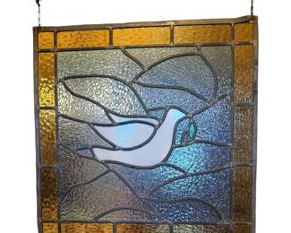 This handmade stained glass panel depicts a white dove of peace in flight carrying an olive branch, bordered by a textured amber and yellow glass frame. It has a sticker on it that says Memphis Tennessee 1979.